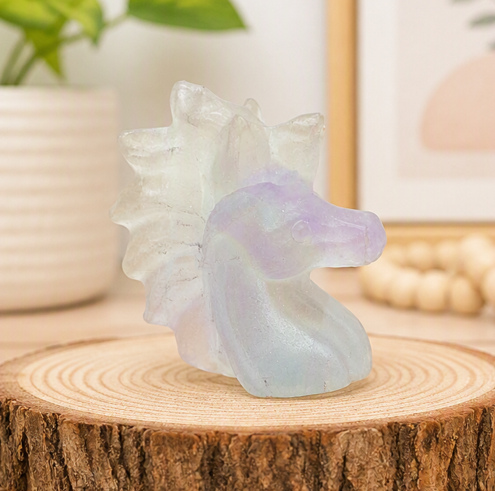 Natural rainbow fluorite unicorn figurine displayed on wood slice in bright indoor décor, showing clear, green, and purple color transitions-My Aura Gemstones