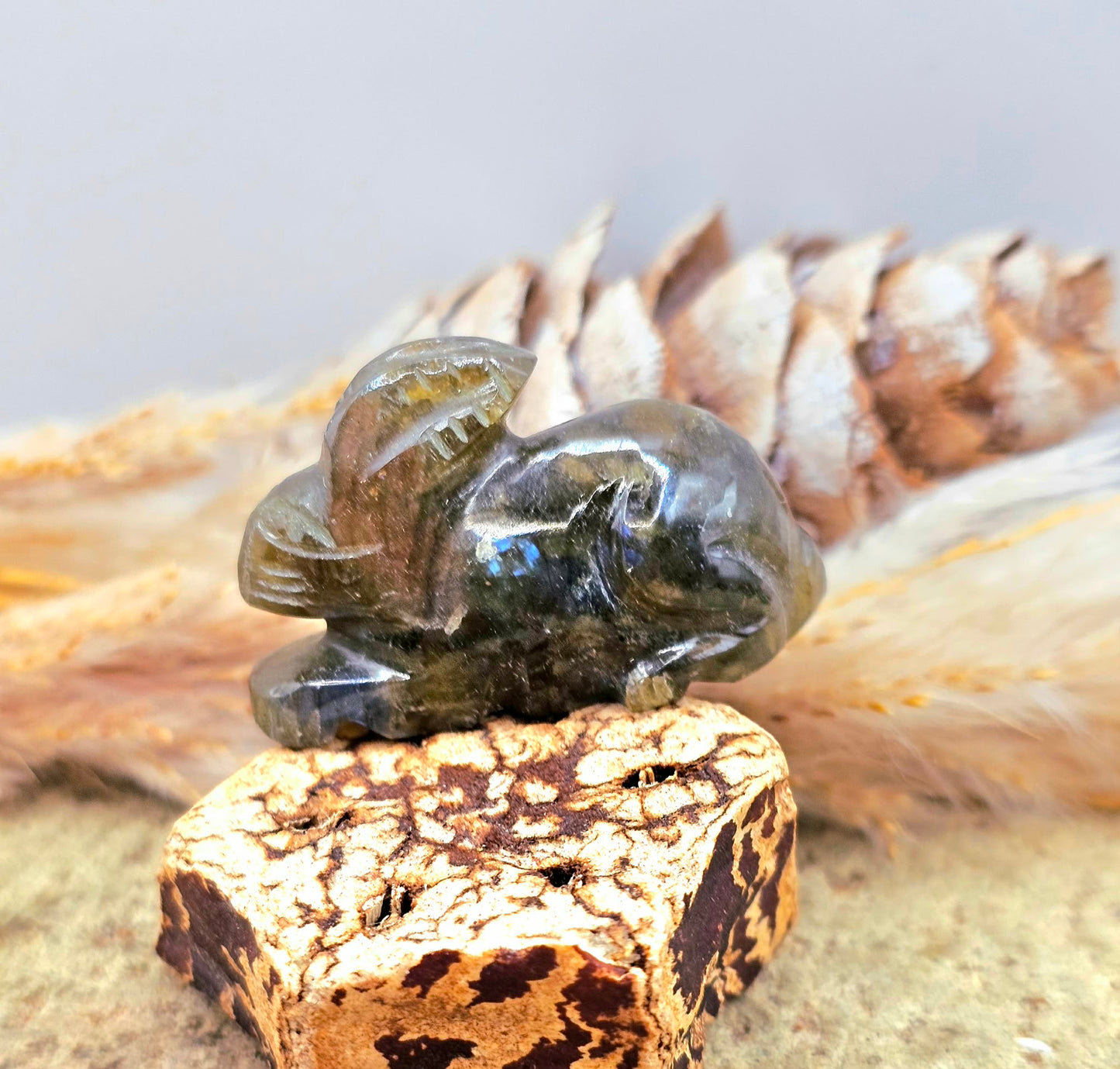 One hand carved rabbit figurines displayed on a natural wood slice, with a pinecone and dried grass in the background.