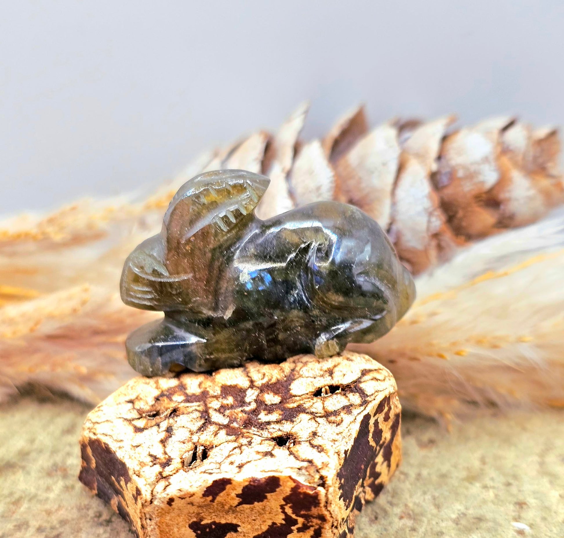 One hand carved rabbit figurines displayed on a natural wood slice, with a pinecone and dried grass in the background.