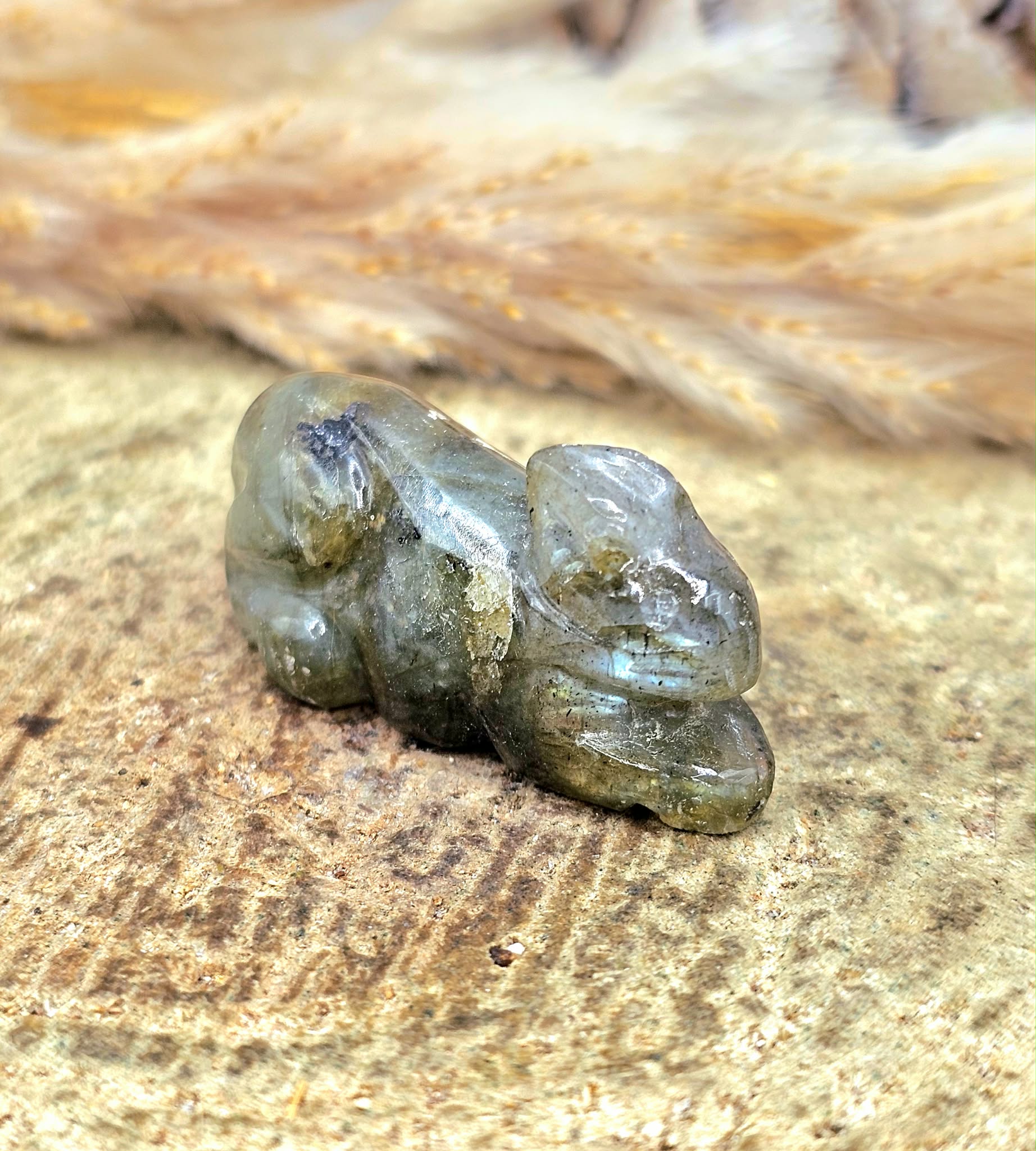 One hand carved rabbit figurines displayed on a natural wood slice, with a pinecone and dried grass in the background.