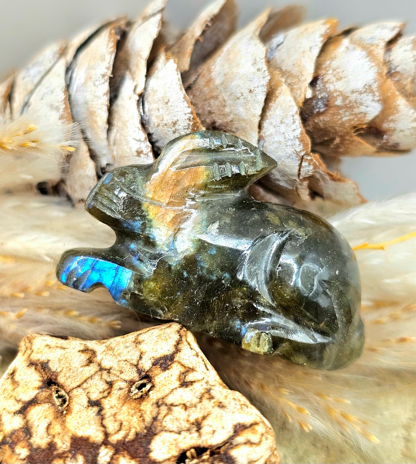 One hand carved rabbit figurines displayed on a natural wood slice, with a pinecone and dried grass in the background.