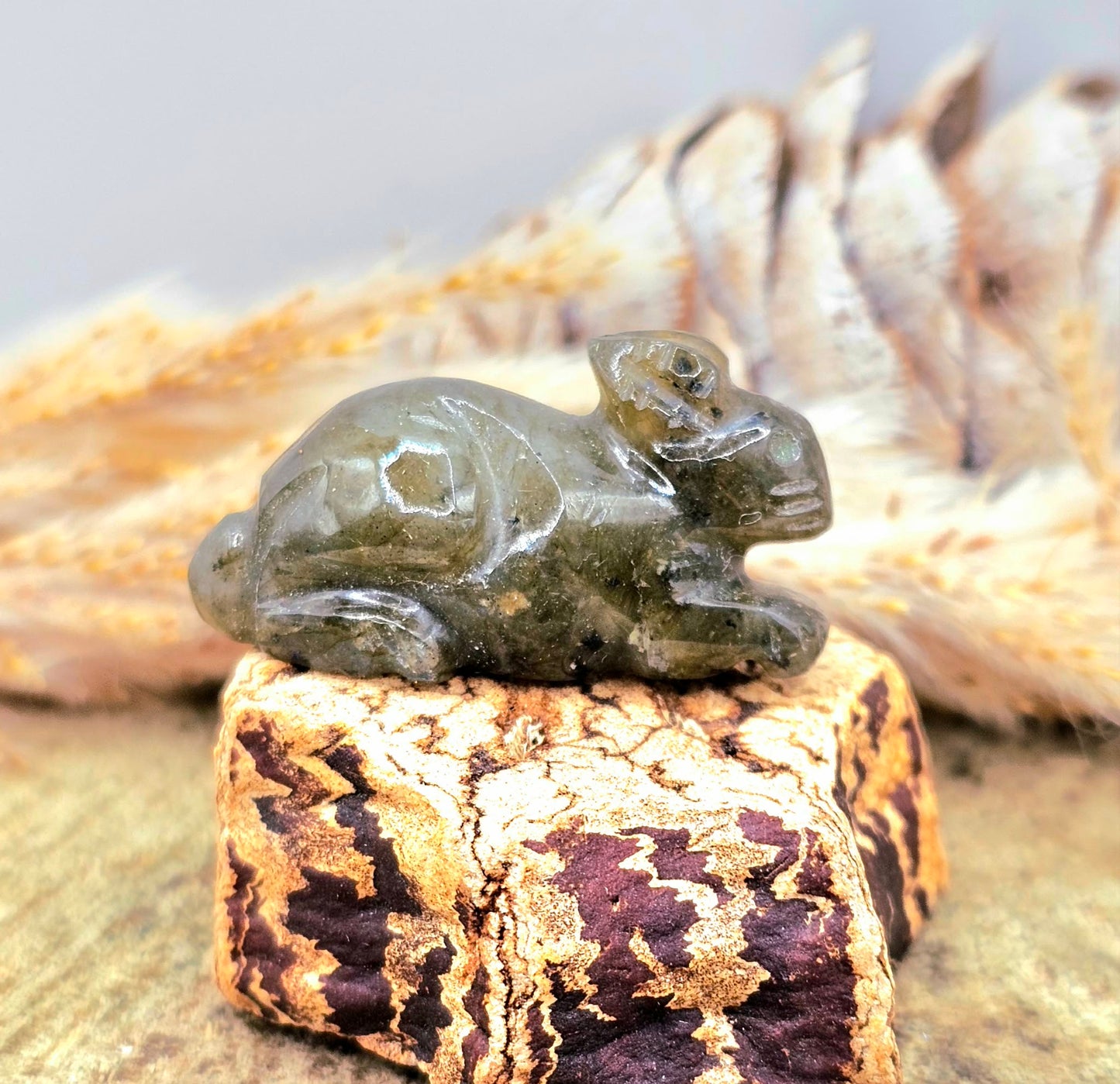 One hand carved rabbit figurines displayed on a natural wood slice, with a pinecone and dried grass in the background.