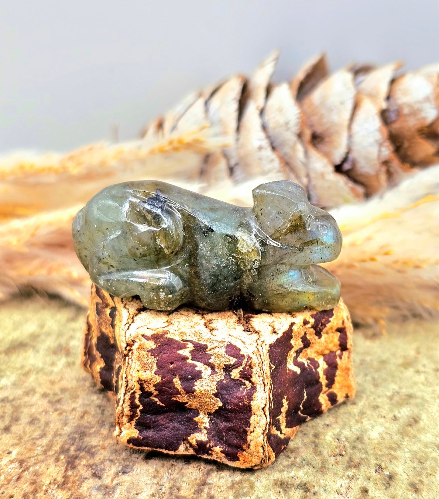 One hand carved rabbit figurines displayed on a natural wood slice, with a pinecone and dried grass in the background.