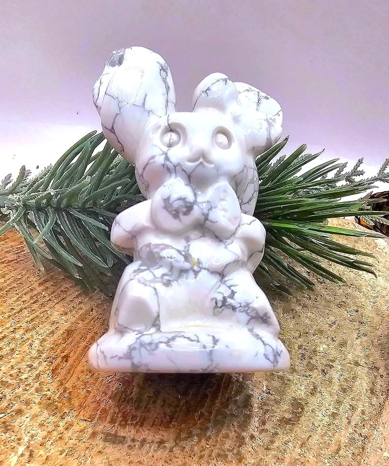 A white howlite carved figurine of a rabbit with gray veining, styled on a textured wooden surface