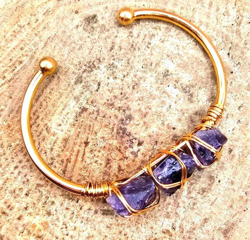 A handmade cuff bracelet featuring three rough purple amethyst stones wrapped in gold-toned wire bangle in top view My Aura Gemstones