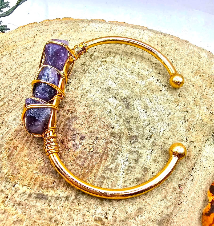 A handmade cuff bracelet featuring three rough purple amethyst stones wrapped in gold-toned wire bangle in side view My Aura Gemstones