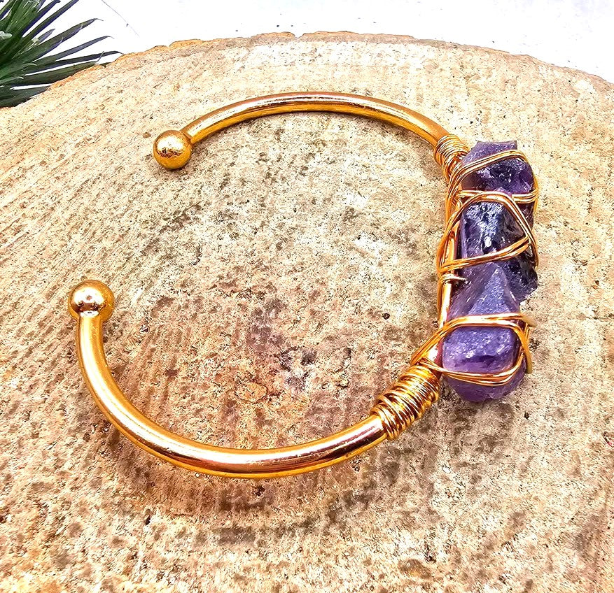 A handmade cuff bracelet featuring three rough purple amethyst stones wrapped in gold-toned wire bangle in side view My Aura Gemstones