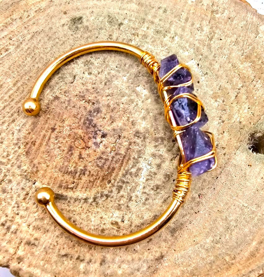 A handmade cuff bracelet featuring three rough purple amethyst stones wrapped in gold-toned wire bangle in another top view My Aura Gemstones