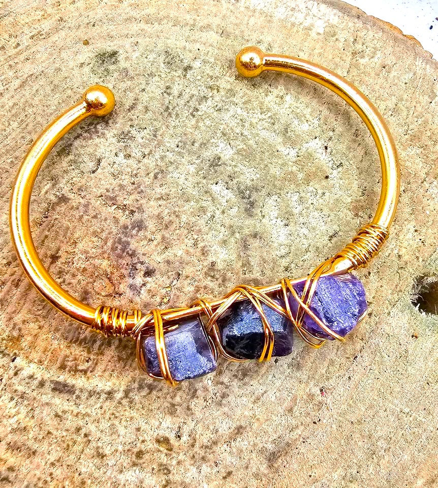 A handmade cuff bracelet featuring three rough purple amethyst stones wrapped in gold-toned wire bangle in another top view My Aura Gemstones