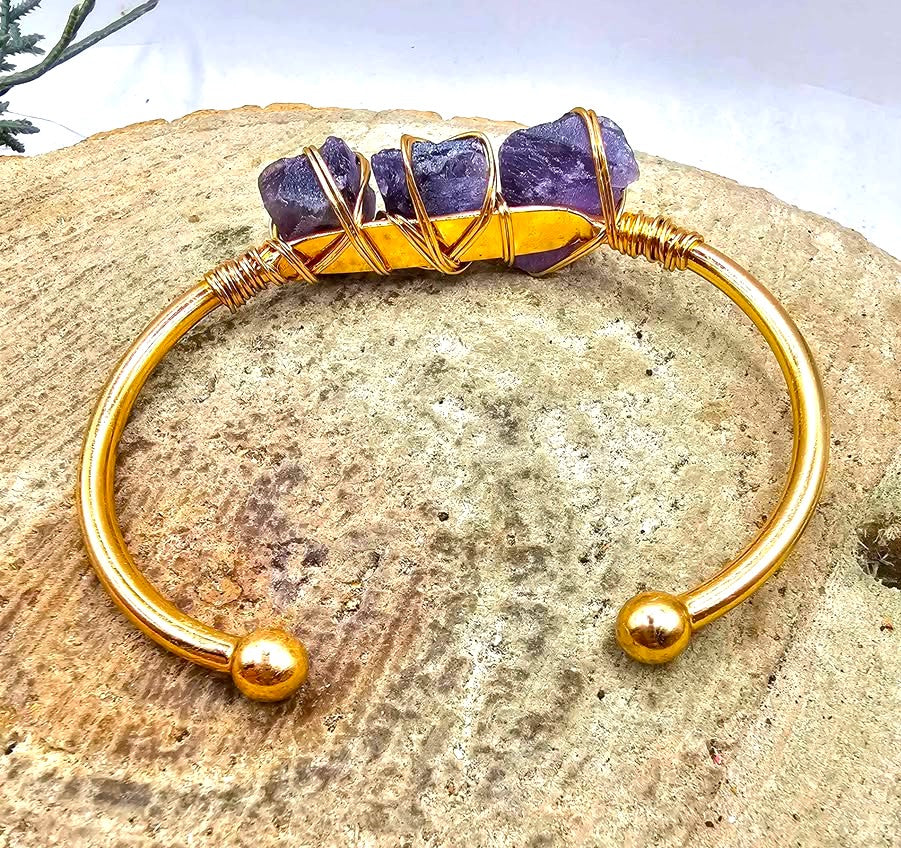 A handmade cuff bracelet featuring three rough purple amethyst stones wrapped in gold-toned wire bangle in back view My Aura Gemstones