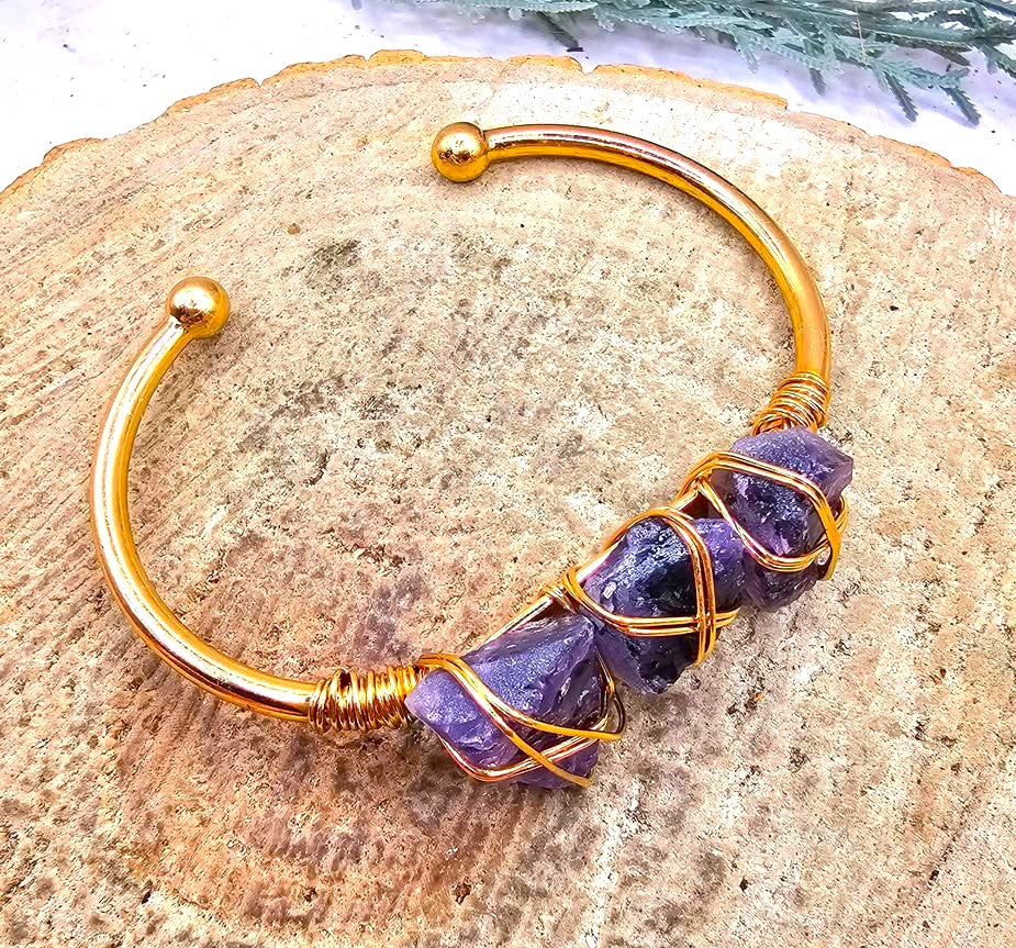 A handmade cuff bracelet featuring three rough purple amethyst stones wrapped in gold-toned wire bangle in  another side view My Aura Gemstones