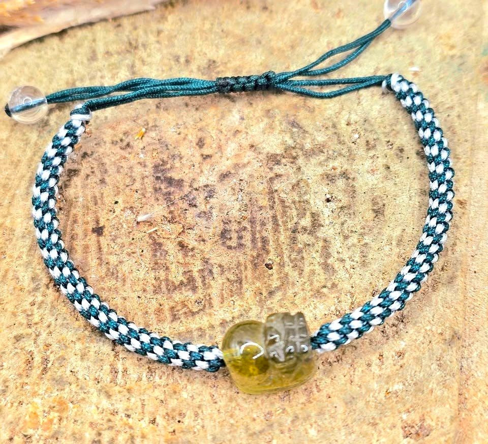 Natural Peridot carved Pi Xiu bracelet with white and dark green braided cord displayed on a white background.