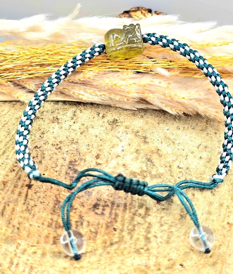 Natural Peridot carved Pi Xiu bracelet with white and dark green braided cord displayed on a white background.