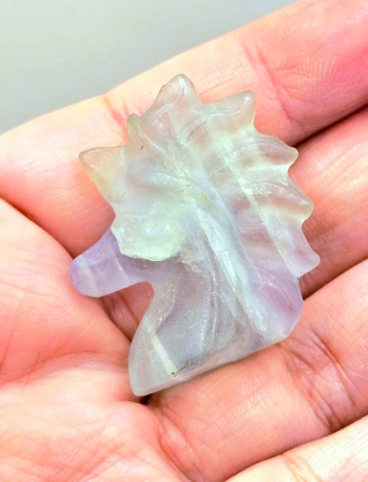 Natural rainbow fluorite unicorn figurine displayed on wood slice in bright indoor décor, showing clear, green, and purple color transitions-My Aura Gemstones