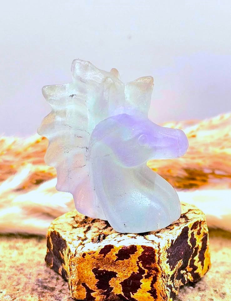 Natural rainbow fluorite unicorn figurine displayed on wood slice in bright indoor décor, showing clear, green, and purple color transitions-My Aura Gemstones