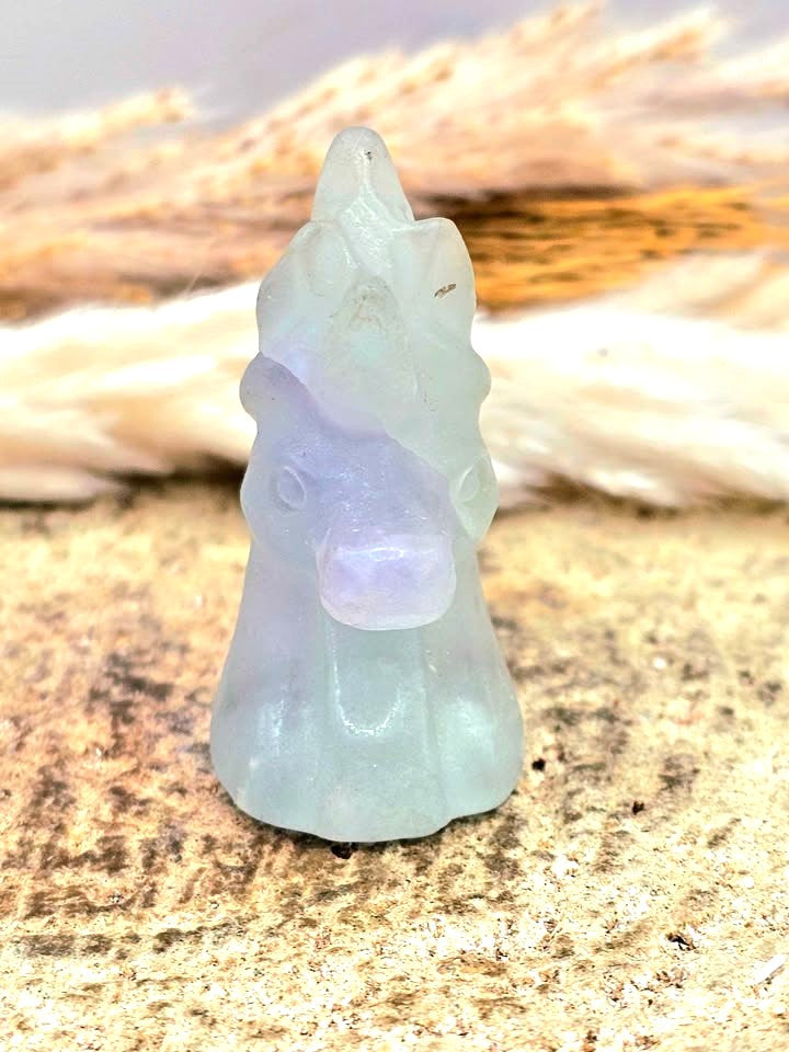 Natural rainbow fluorite unicorn figurine displayed on wood slice in bright indoor décor, showing clear, green, and purple color transitions-My Aura Gemstones