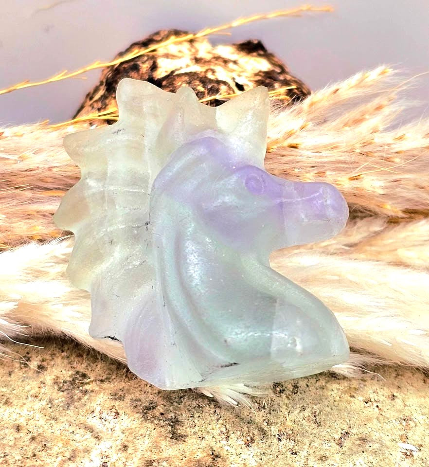 Natural rainbow fluorite unicorn figurine displayed on wood slice in bright indoor décor, showing clear, green, and purple color transitions-My Aura Gemstones