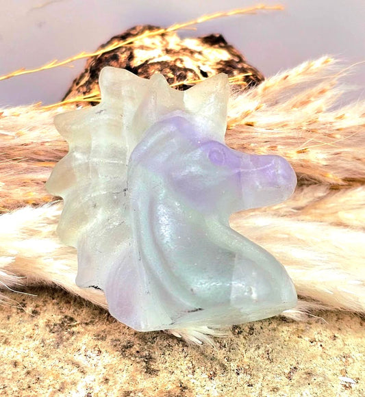 Natural rainbow fluorite unicorn figurine displayed on wood slice in bright indoor décor, showing clear, green, and purple color transitions-My Aura Gemstones