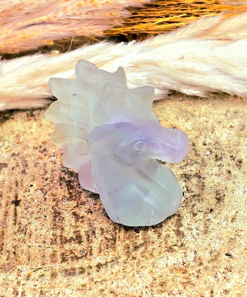 Natural rainbow fluorite unicorn figurine displayed on wood slice in bright indoor décor, showing clear, green, and purple color transitions-My Aura Gemstones