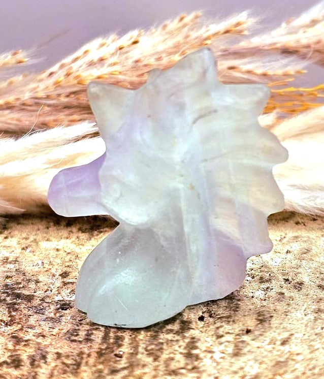 Natural rainbow fluorite unicorn figurine displayed on wood slice in bright indoor décor, showing clear, green, and purple color transitions-My Aura Gemstones