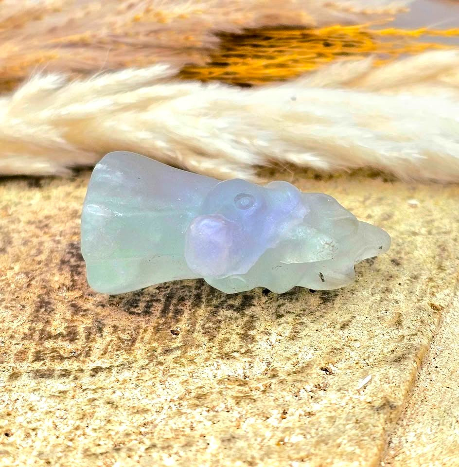 Natural rainbow fluorite unicorn figurine displayed on wood slice in bright indoor décor, showing clear, green, and purple color transitions-My Aura Gemstones