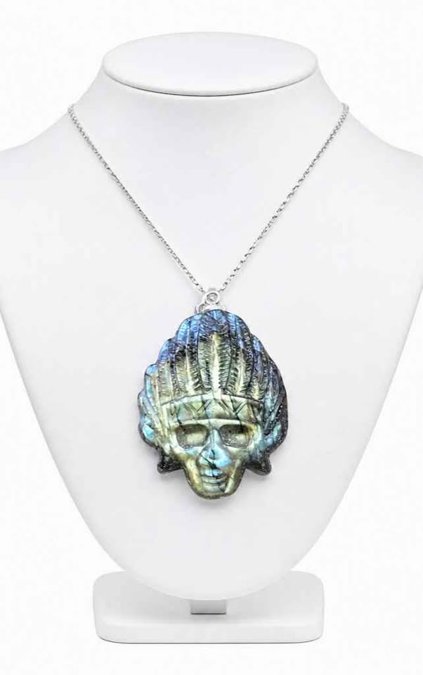 A silver chain necklace with a detailed skull pendant featuring a blue-green iridescent textured finish, displayed on a white mannequin bust.