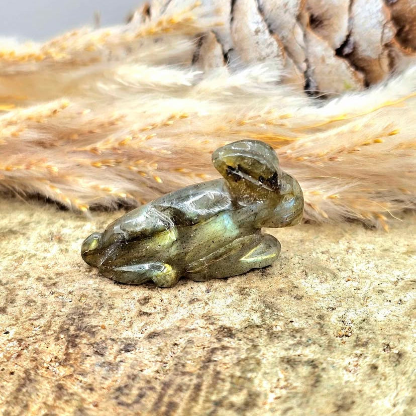 One  hand carved rabbit figurines displayed on a natural wood slice, with a pinecone and dried grass in the background.