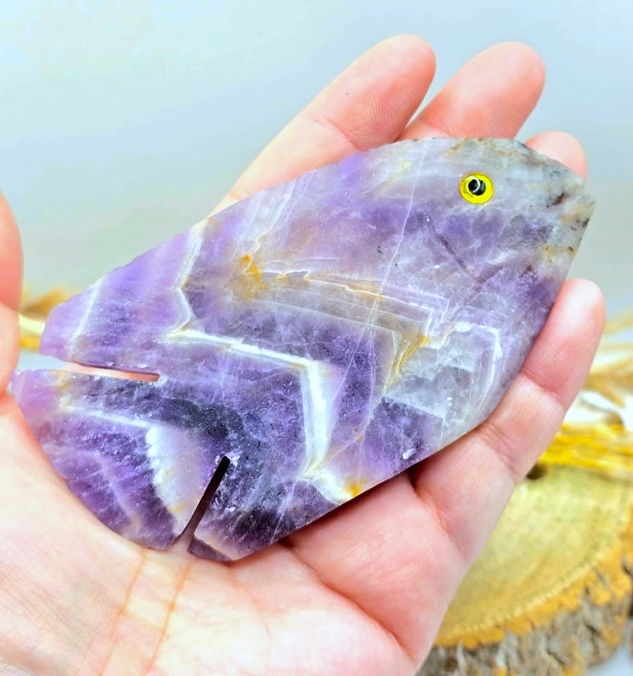 Hand‑carved Dream Amethyst fish figurine with chevron pattern and purple quartz, 4.1 inch crystal carving, display on hand-My Aura Gemstones