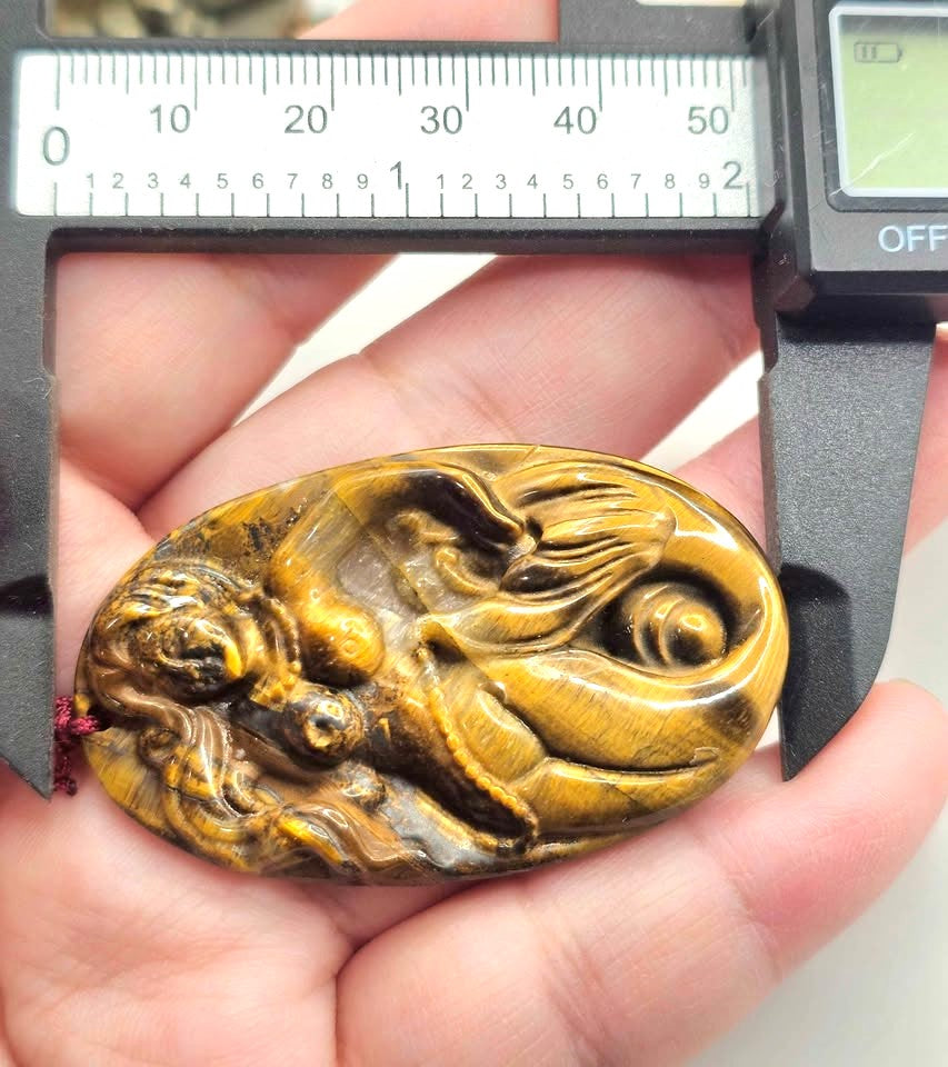 A carved oval pendant made of golden-brown tiger's eye stone carved mermaid,  pendant threaded on a red cord with a red bead-My Aura Gemstones