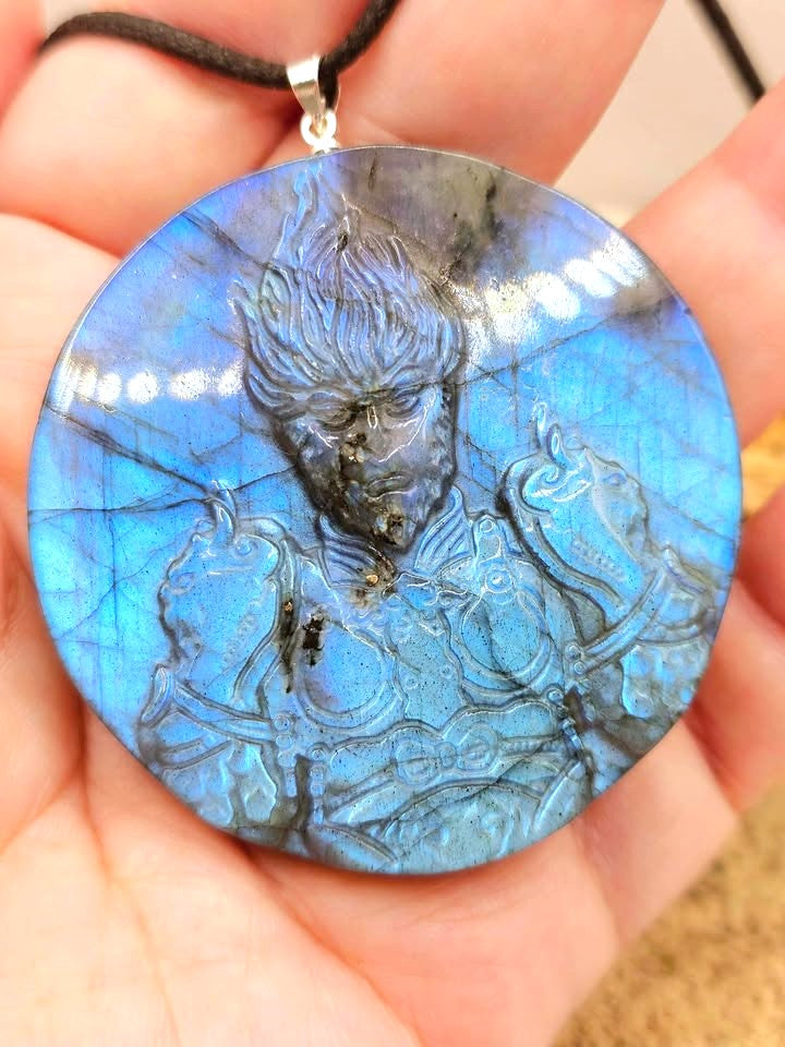 A labradorite carved round pendant necklace featuring a carved of powerful monkey king in front view on a wood slice display on hand-My Aura Gemstones