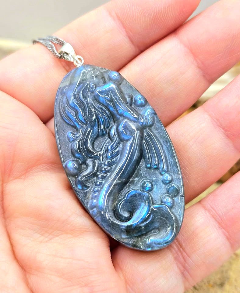 Labradorite carved pendant featuring a mermaid design, suspended from a silver chain, displayed on hand Aura Gemstones