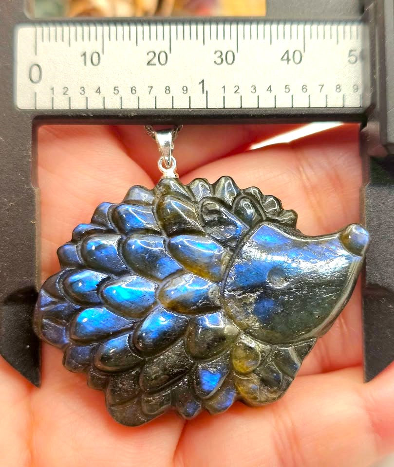 A carved labradorite hedgehog pendant with a silver bail, resting on hand with measurement-My Aura Gemstones