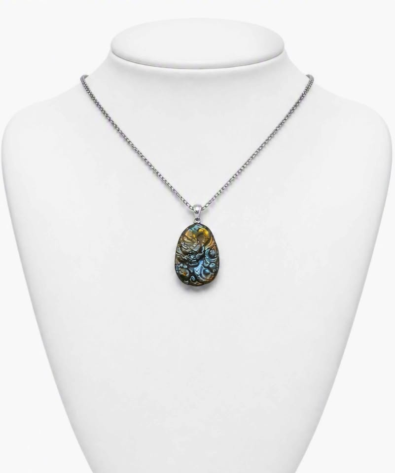 A silver chain necklace with a teardrop-shaped pendant featuring a highly iridescent, patterned shell-like design in blue, gold, and green, displayed on a white neck mannequin.