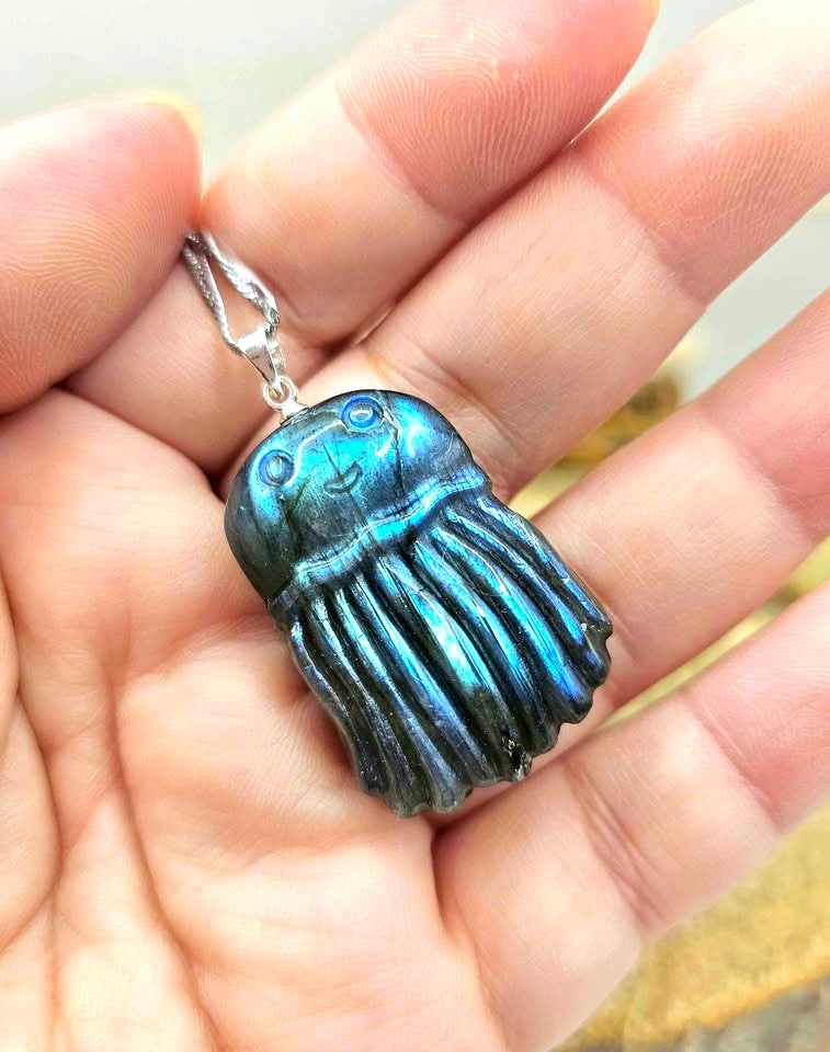 A blue iridescent jellyfish pendant necklace with a silver bail and chain, resting on human hand-My Aura Gemstones