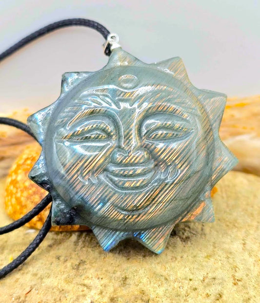 A labradorite carved metal sun pendant with a smiling face and pointed rays, hanging from a black cord. The pendant has a textured, brushed metallic finish in a silver-gray tone-My Aura Gemstones