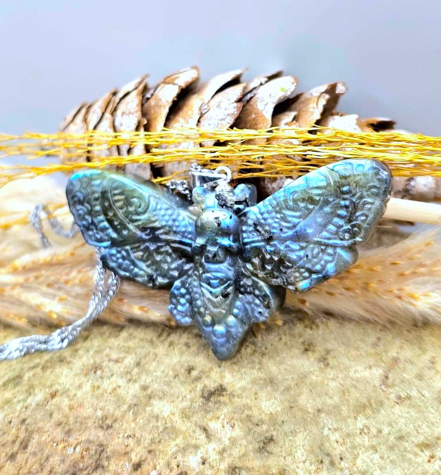 Natural Labradorite Moth With Skull Pendant Necklace displays on wood slice at side view-My Aura Gemstones