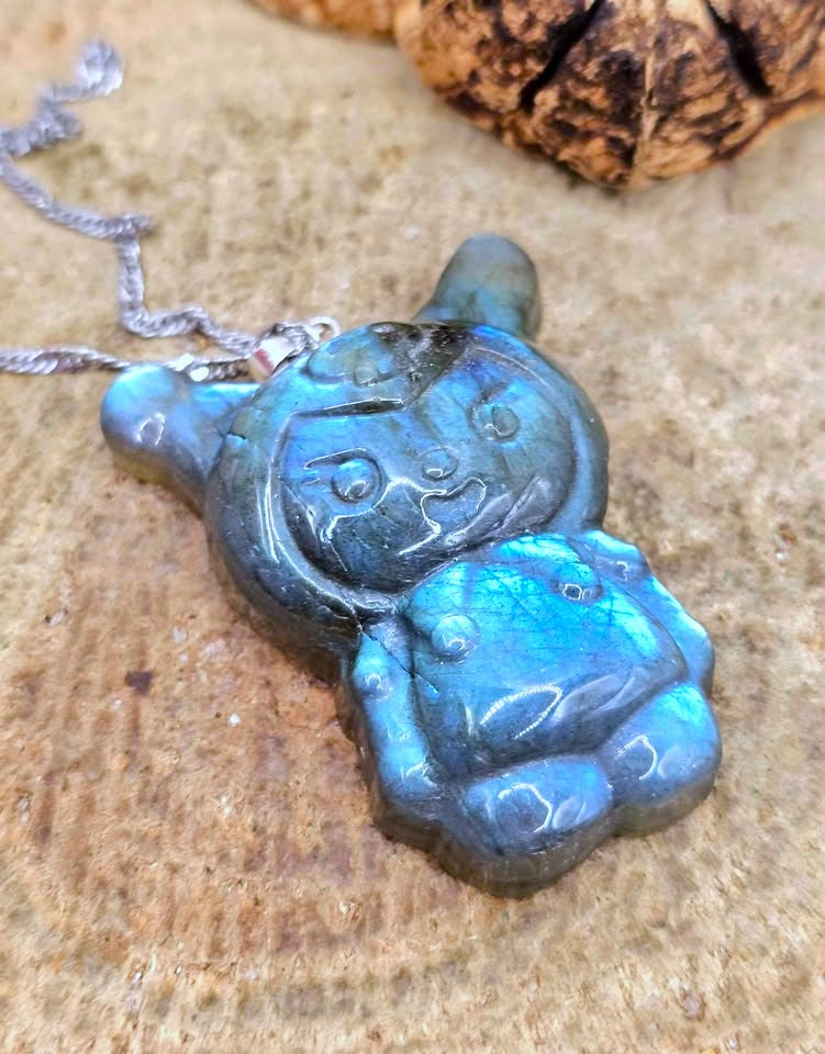Natural labradorite pendant featuring a Kuromi‑inspired carving with smile and skull detail with silver chain displays on wood slice-My Aura Gemstones