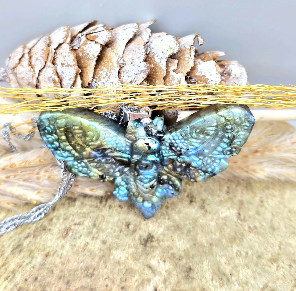 Natural Labradorite Moth With Skull Pendant Necklace displays on wood slice at top view-My Aura Gemstones