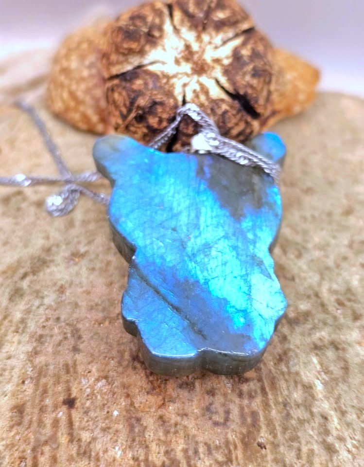 Natural labradorite pendant featuring a Kuromi‑inspired carving with smile and skull detail with silver chain displays on wood slice at back view-My Aura Gemstones