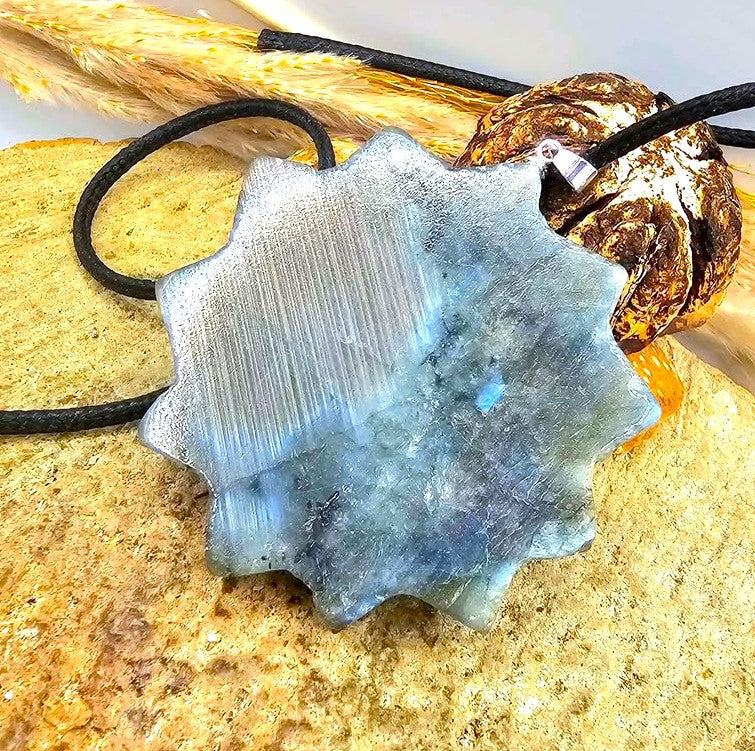 A labradorite carved metal sun pendant with a smiling face and pointed rays, hanging from a black cord. The pendant has a textured, brushed metallic finish in a silver-gray tone in back side-My Aura Gemstones