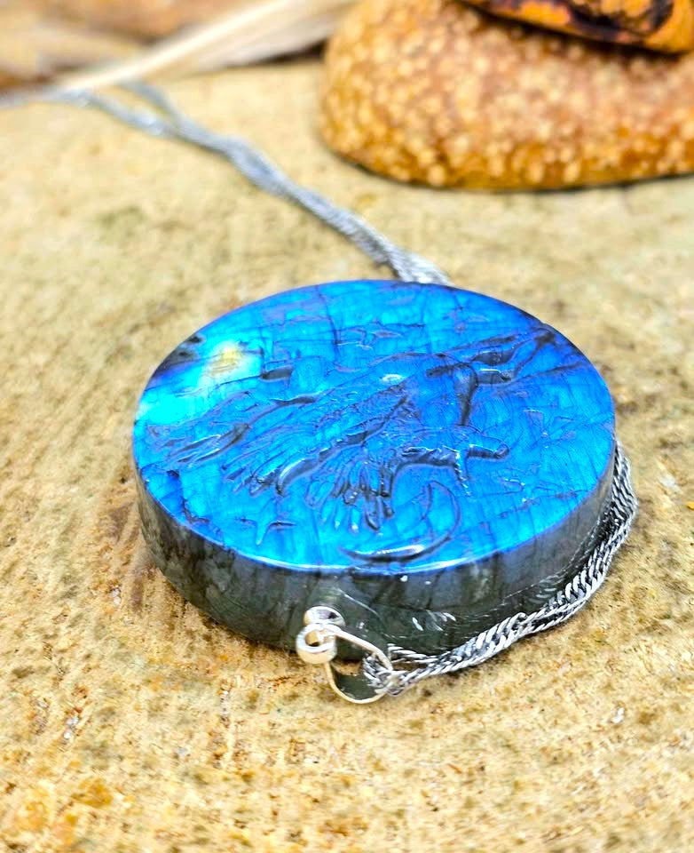 A round cabochon pendant necklace featuring a vibrant blue and black marbled pattern, suspended from a silver chain and resting on a textured stone surface.