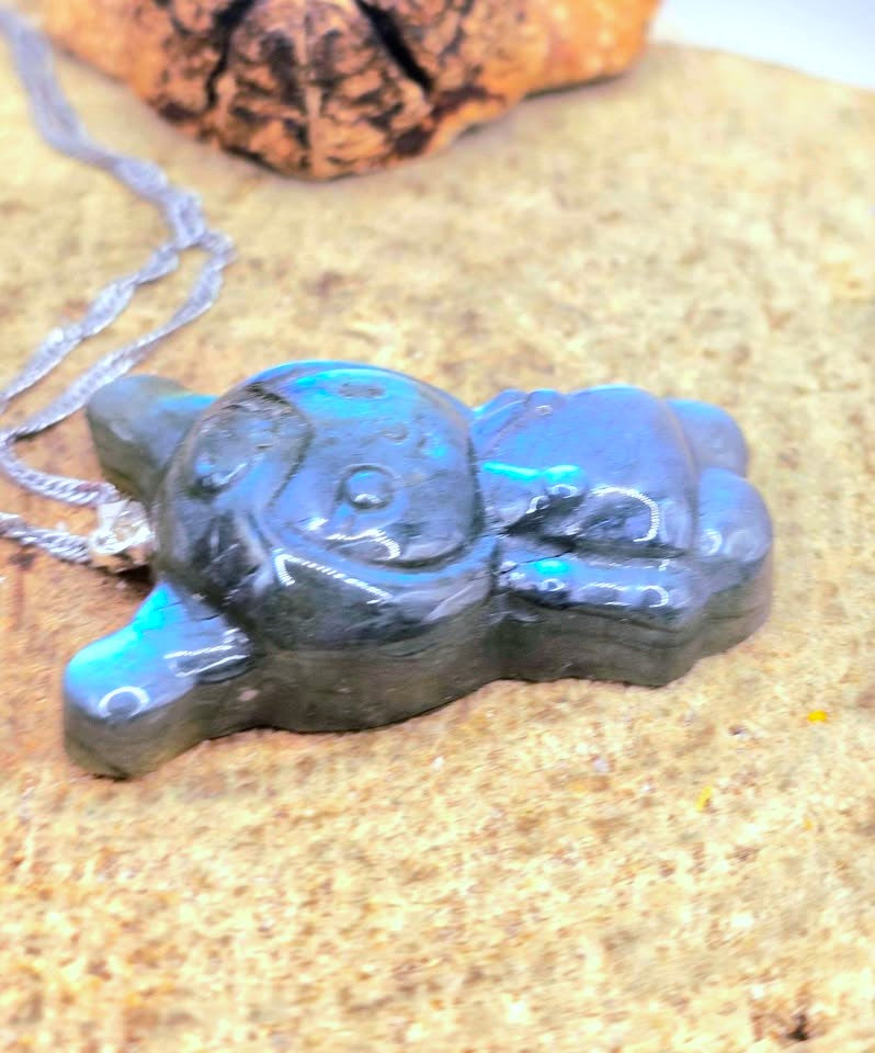 Natural labradorite pendant featuring a Kuromi‑inspired carving with smile and skull detail with silver chain displays on wood slice at side view-My Aura Gemstones