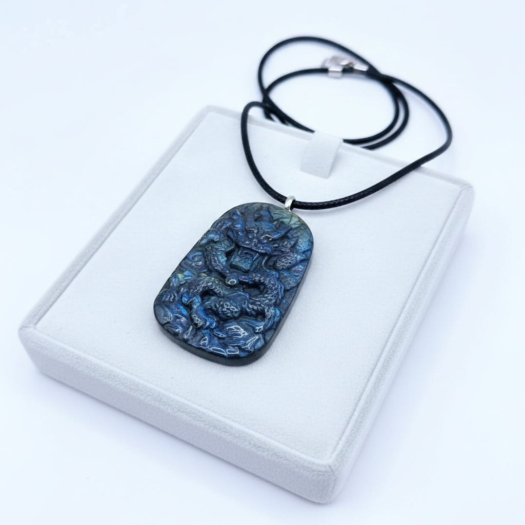 A carved labradorite pendant necklace with a black cord, featuring a detailed relief carving of a figure, displayed on a textured wood surface.