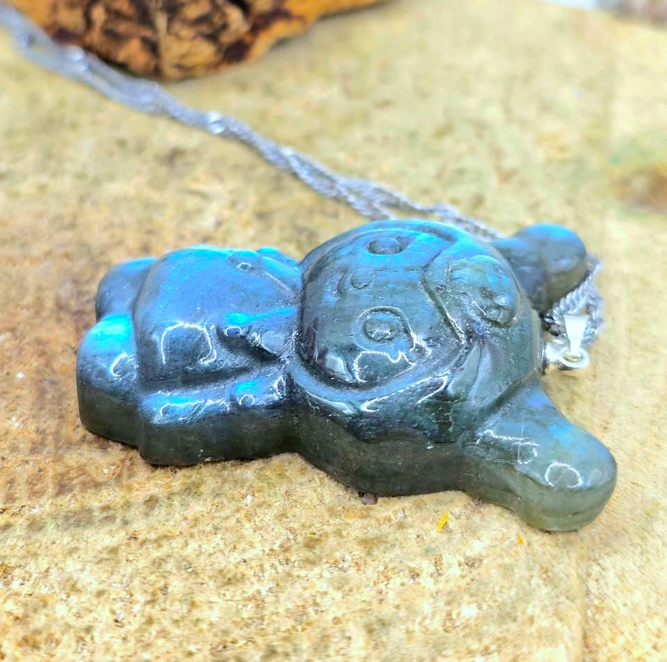 Natural labradorite pendant featuring a Kuromi‑inspired carving with smile and skull detail with silver chain displays on wood slice at another side view-My Aura Gemstones
