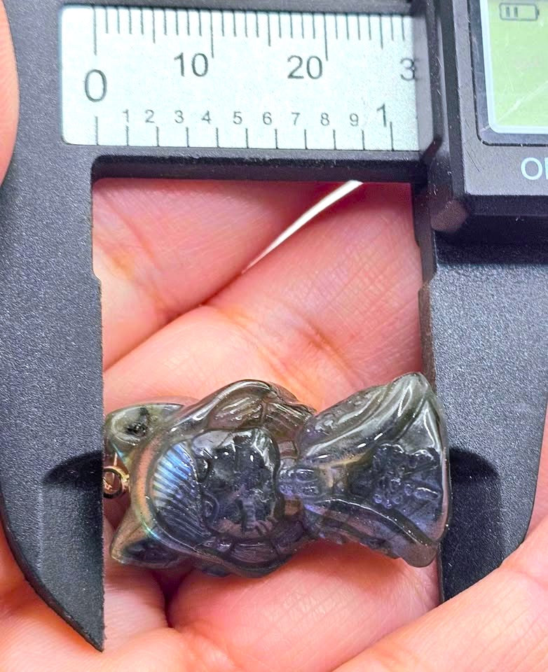 A blue iridescent pendant necklace shaped like a hooded figure, shown close up against a textured brown rock background with part of a silver chain visible.-My Aura Gemstones