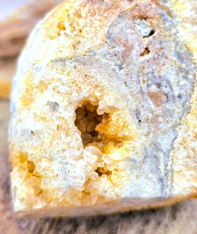 A close-up of a natural crystal geode specimen with a hollow cavity lined with golden-yellow quartz crystals, surrounded by a rough beige and gray outer matrix.
