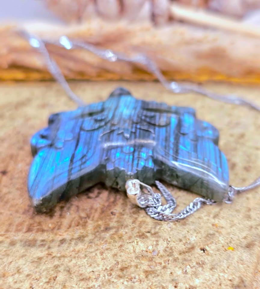 A star-shaped labradorite pendant necklace with a silver-toned chain, resting on a textured stone surface.