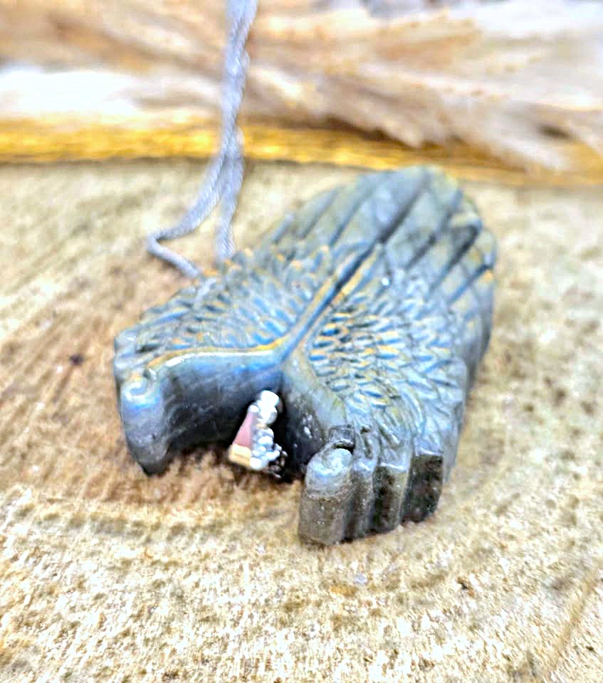 A small carved dark gray stone pendant shaped like a stylized hand, with a gray cord attached, resting on a textured tan surface.
