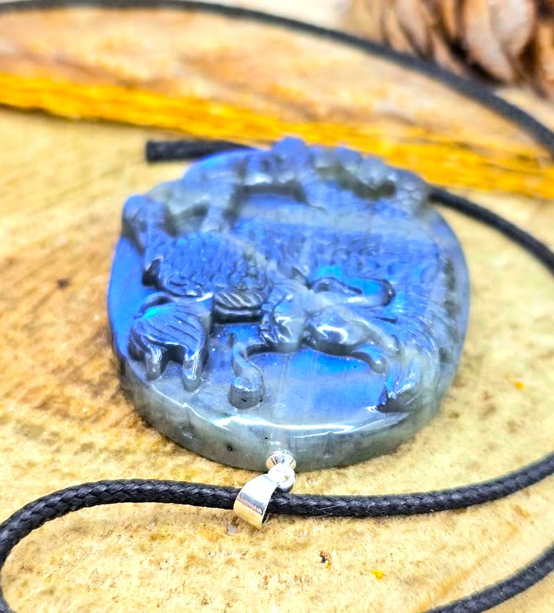 A carved blue stone pendant with foo dog design, hanging from a black cord with a silver-toned metal clasp, displayed on a textured wooden surface.