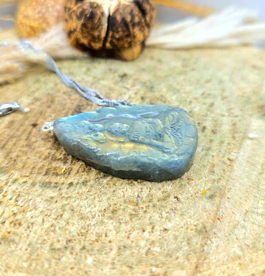 A carved stone pendant necklace with a silver bail, resting on a textured beige surface with a blurred background.